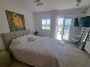 Quarto com cama grande, pintura na parede, TV e vista para o exterior.