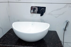 Un lavabo blanco sobre una encimera de granito en un baño con pared de mármol y dispensador de toallas.