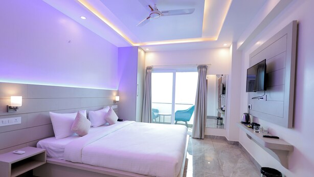A modern hotel room with a large bed, bedside tables, a TV, and a balcony with a view. - GREEN HILLS HOTEL (Pithoragarh)