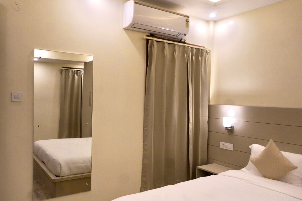A hotel room with a bed, a mirror, a wall-mounted air conditioner, and a curtain.