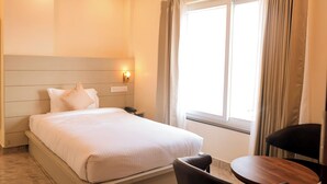 A hotel room with a bed, bedside table, lamp, chair, and a window with curtains. - GREEN HILLS HOTEL (Pithoragarh)
