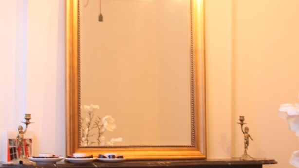 Un espace repas agrémenté d’un grand miroir, d’un lustre et d’une cheminée en marbre.