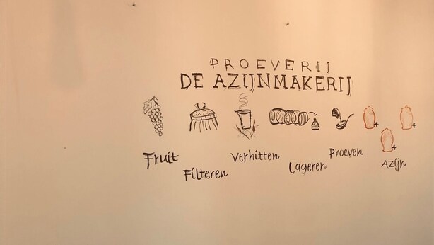 Una mesa de comedor dispuesta con copas de vino, cubiertos y un bol, con una pared decorada con una ilustración de preparación de alimentos.