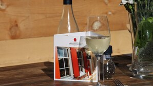 Une table avec une bouteille de vin, un verre, un menu et un vase de fleurs.