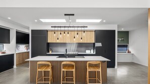 A modern kitchen with a central island, three wooden chairs, and pendant lighting. - Villa Hitam - Burleigh Heads (Gold Coast)