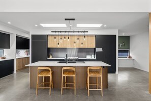 A modern kitchen with a central island, three wooden chairs, and pendant lighting.