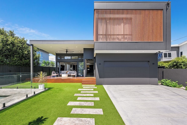 A modern two-story house with a covered patio, a garage, and a well-maintained lawn with stepping stones.