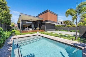 A modern house with a swimming pool, a covered outdoor seating area, and a well-maintained garden.