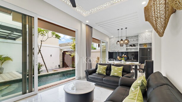 A modern living room with a black sofa, a round coffee table, and a view of a swimming pool and outdoor area.