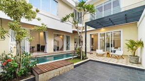 A modern outdoor patio with a swimming pool, seating area, and potted plants.