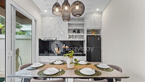 A modern dining area with a glass table, grey upholstered chairs, and a white vase with a plant.