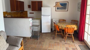 Cozinha compacta com armários de madeira, geladeira branca e área de refeições com mesa e cadeiras.