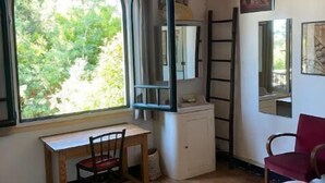 A room with a wooden ceiling, a desk with a chair, a bed with a pink blanket, a window with a view of greenery, and a mirror on the wall. - House in Cap Ferret, Canon village, just a few minutes walk from the beach! (Lège-Cap-Ferret)