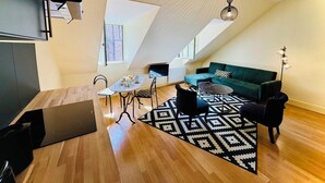 Un appartement moderne de style « loft », avec un plafond haut, un coin repas agrémenté d’un tapis à motifs noir et blanc, un canapé vert et un fauteuil noir.