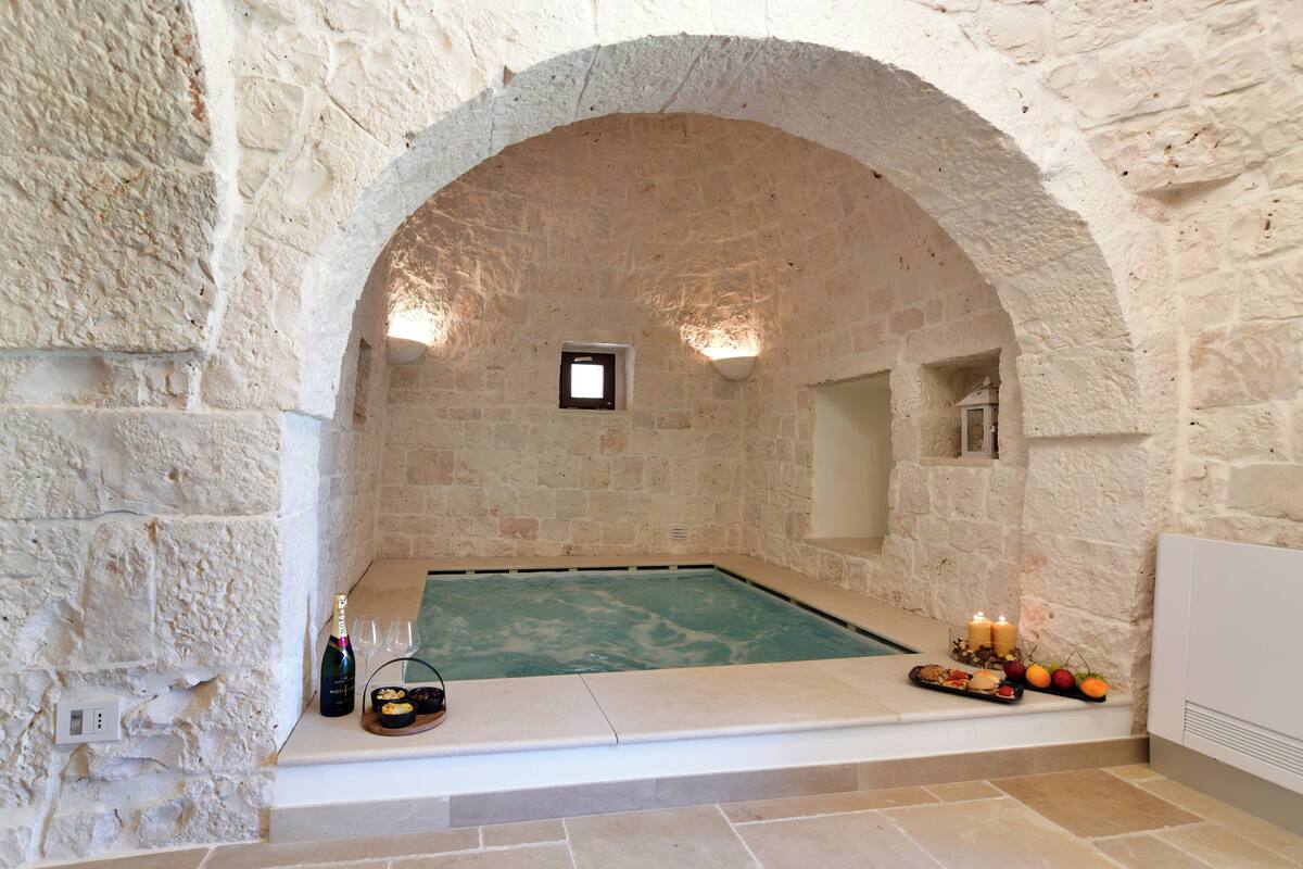 Uma área de spa com paredes de pedra, piscina, velas e petiscos.