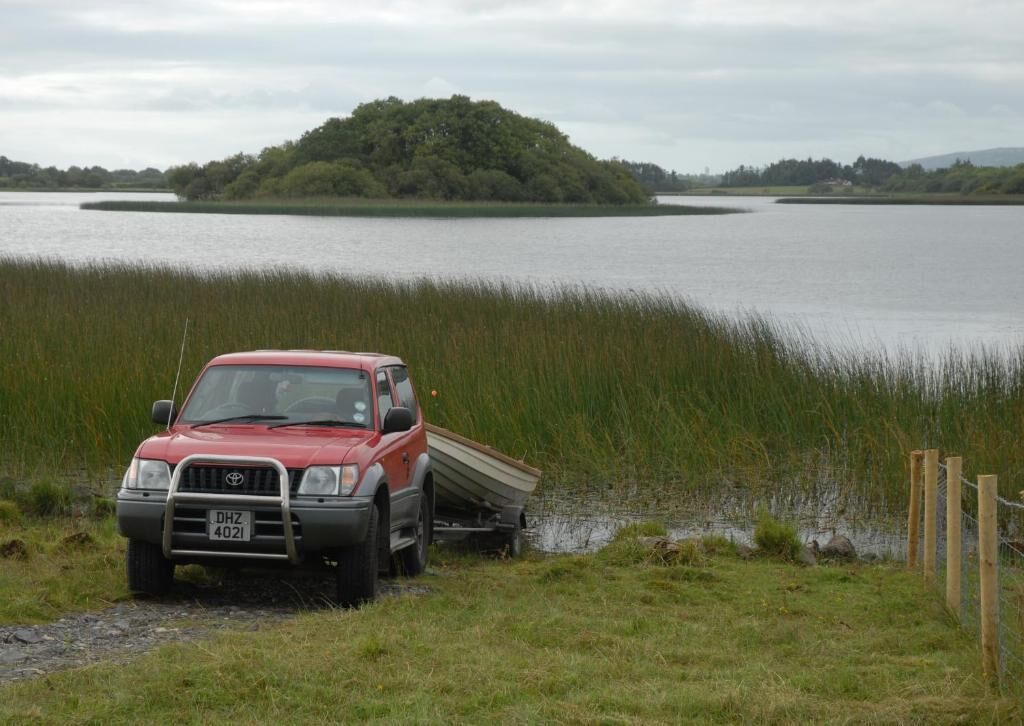 A red SUV parked by a lake with a boat on the back.