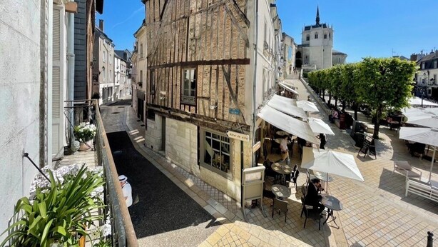 A narrow street with a building featuring exposed timber framing, outdoor seating with umbrellas, and a church spire in the background. - La Chapelle, exceptional view of the castle square with balcony (Amboise)