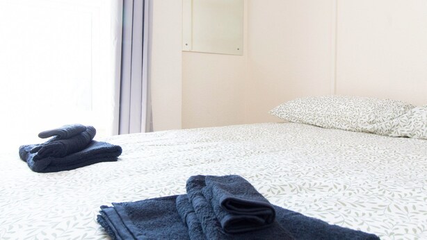 A hotel room with a neatly made bed, a pillow, and folded towels on the bed. - Brookvale Guest House Room 10 (Southampton)