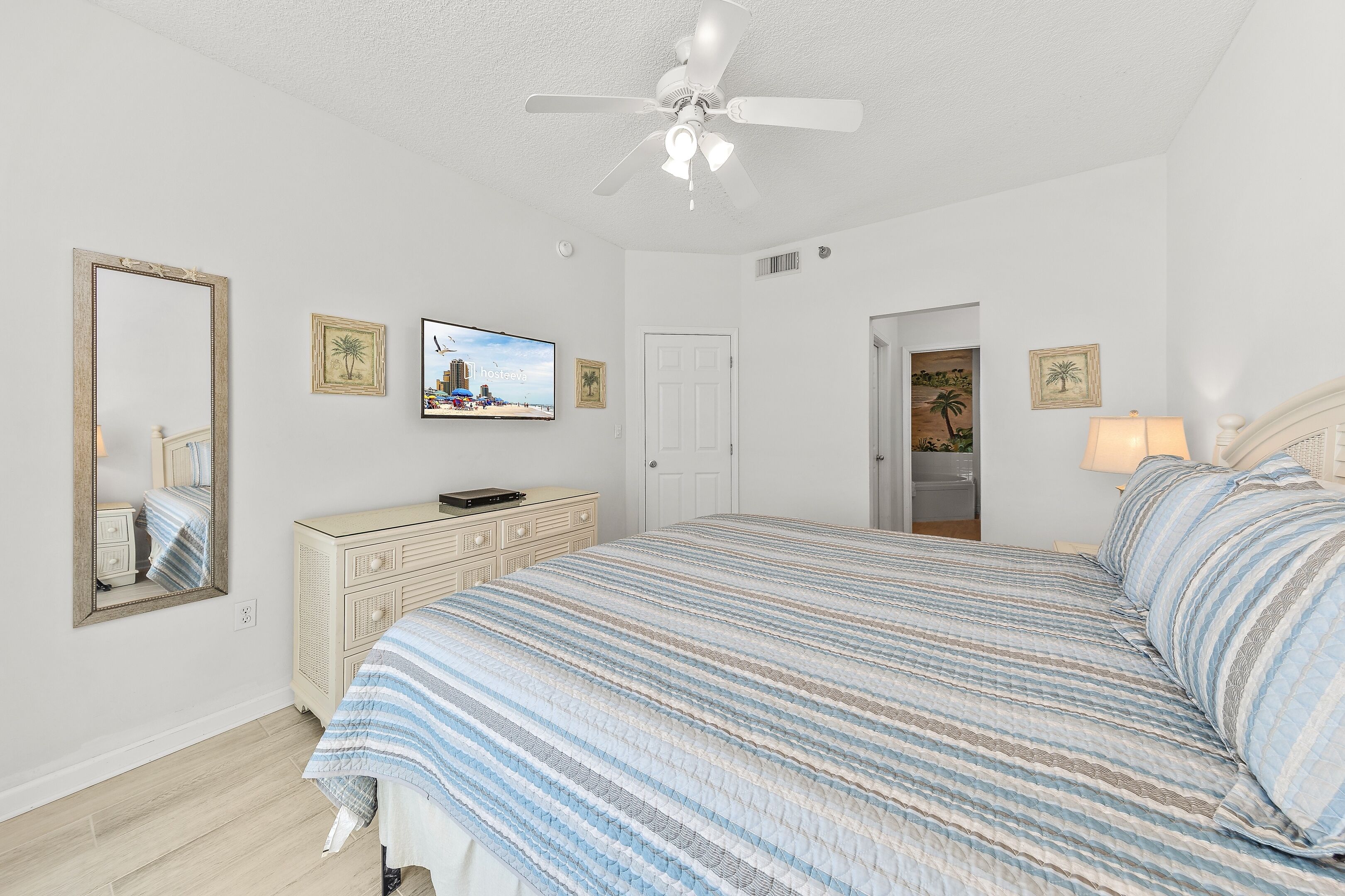 A bedroom with a bed, a ceiling fan, a dresser, a television, and framed pictures on the wall.