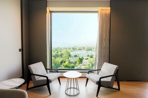 A modern room with two grey armchairs, a small white table, and a large window with a view of greenery and buildings. - Radisson Hotel Jamshedpur (Jamshedpur)