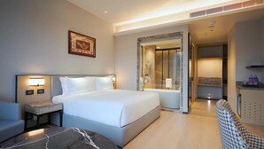 A hotel room with a large bed, bedside tables, a mirror, a small seating area, and a bathroom visible through an open door.
