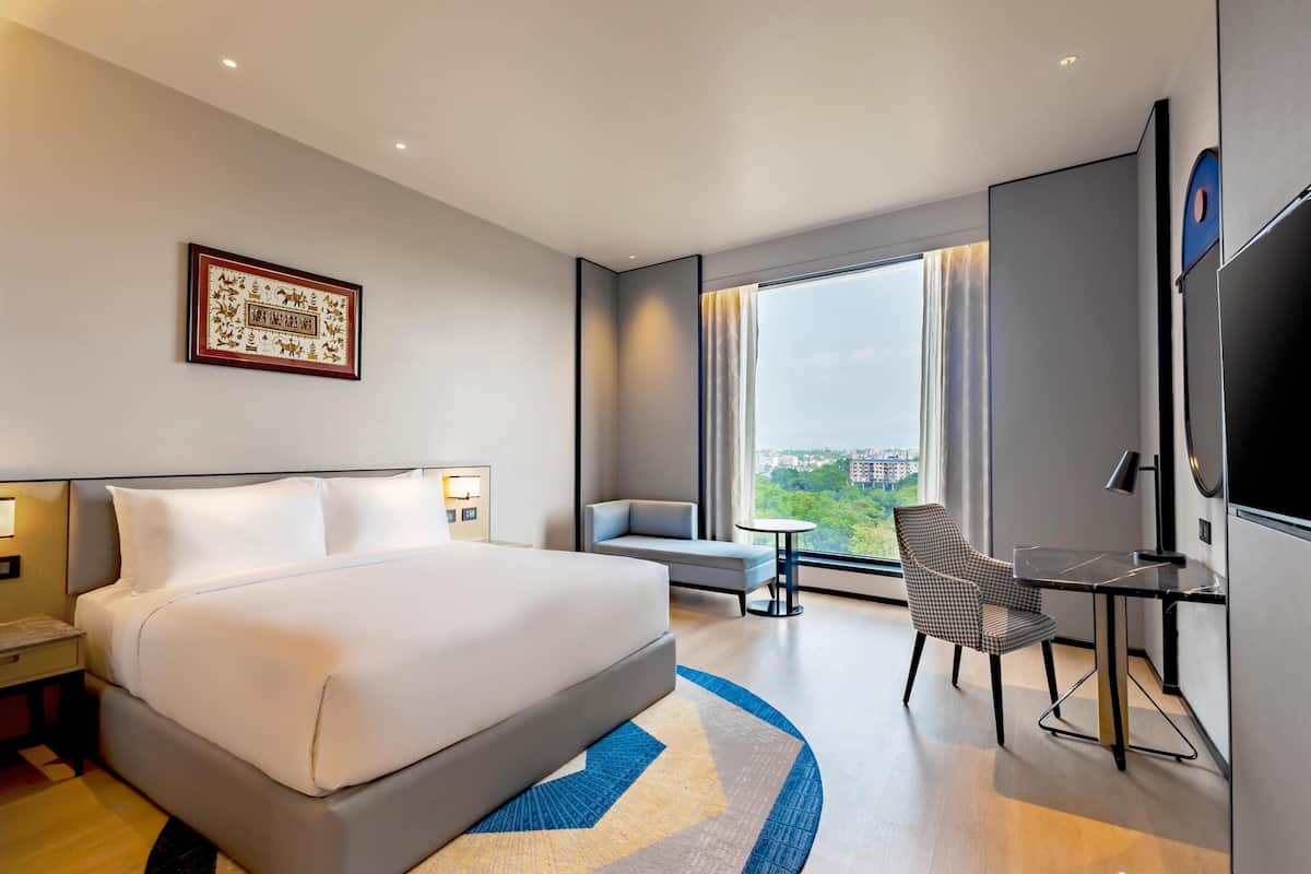 Habitación de hotel moderna con una cama grande, un escritorio con silla, televisión y ventana con vista a la ciudad.