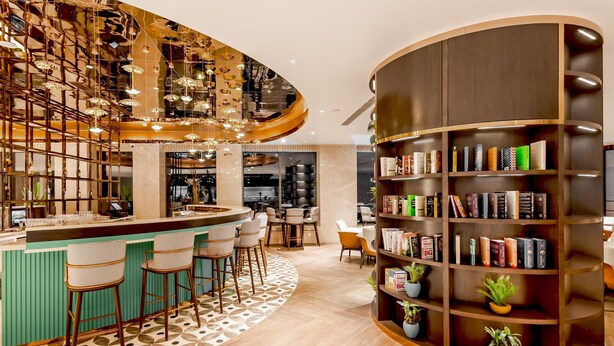 A modern bar area with a curved bookshelf filled with books and potted plants.