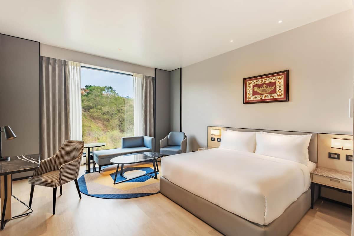 Una habitación de hotel moderna con una cama grande, un escritorio, dos sillas y una mesita pequeña.