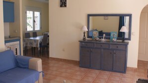 A living room with a sofa, a dining area with chairs and a table, a kitchen with a stove, and a large mirror above a cabinet. - Andalusian vacations (San Juan de los Terreros)