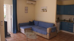 A compact living space with a sofa, a glass coffee table, and a kitchenette area. - Andalusian vacations (San Juan de los Terreros)