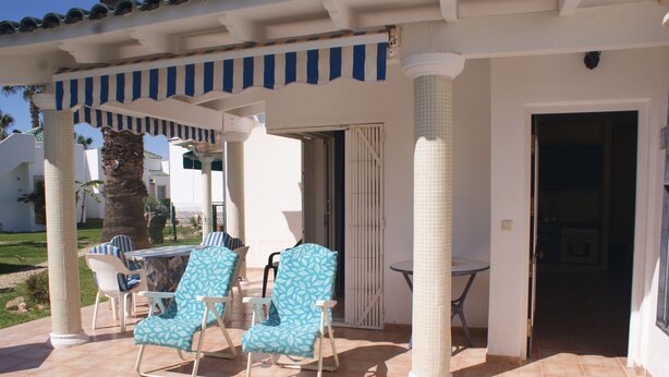 An outdoor patio with two lounge chairs and a table, a covered area with a striped awning, and a door leading to an interior space. - Andalusian vacations (San Juan de los Terreros)