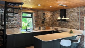 Une cuisine moderne avec un mur en pierre, un plafond en bois et un grand îlot central doté de tabourets de bar.