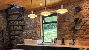 Une cuisine moderne dotée d’un grand îlot central, de tabourets de bar, d’un mur en pierre et d’une fenêtre donnant sur un paysage verdoyant.