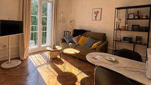 Ein Wohnzimmer mit einer Couch, zwei kleinen Tischen, einem Fernseher und einem Bücherregal.