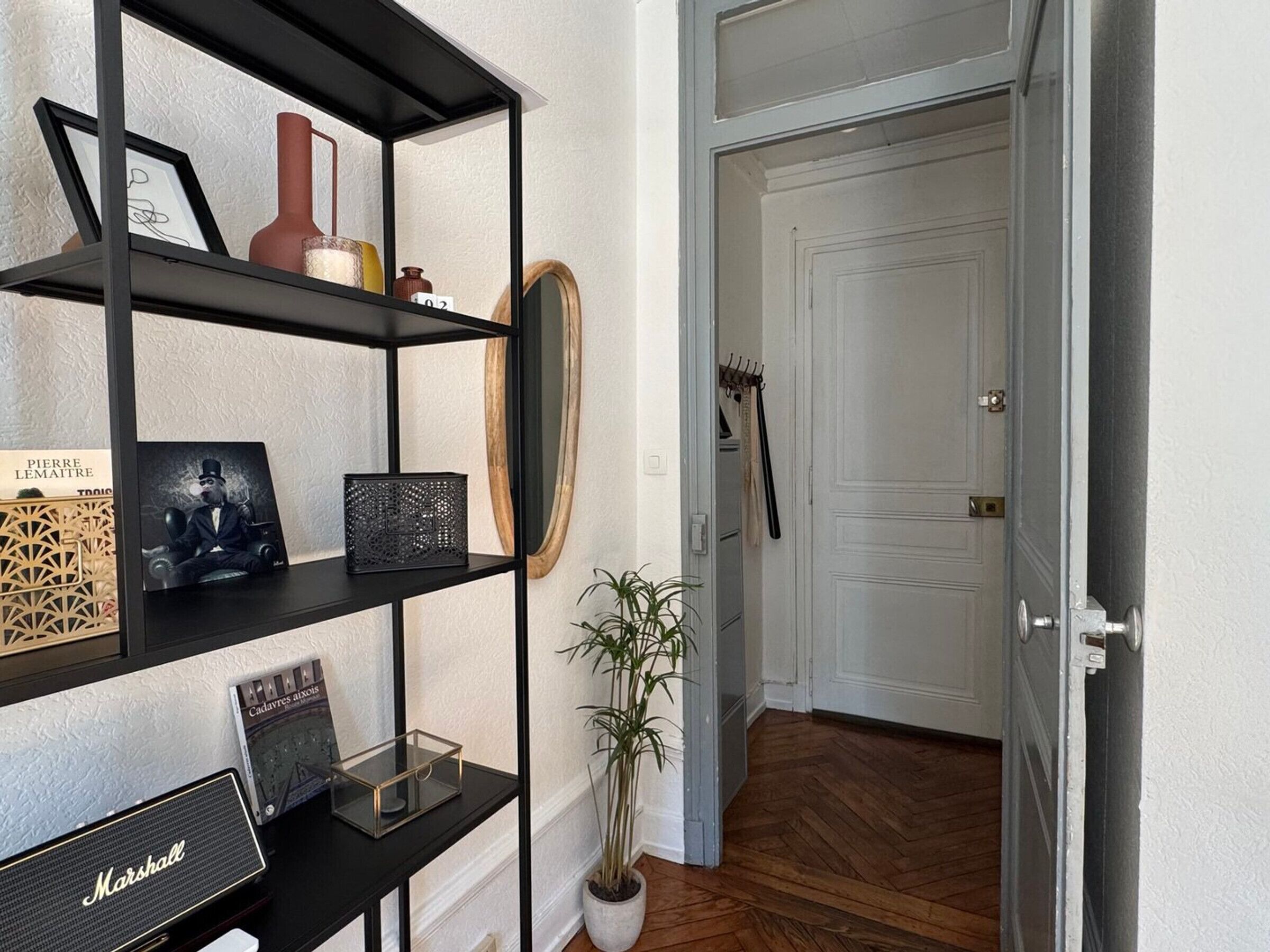 Een gang met een zwarte metalen schapunit waarop diverse decoratieve objecten, een potplant en een Marshall speaker staan.