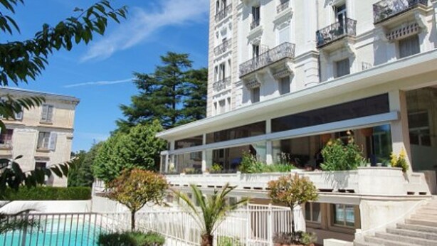 Ein mehrstöckiges Hotel mit Balkonen, einem Schwimmbad und üppiger Vegetation.