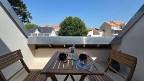 A wooden table with two chairs, a kettle, and a cup on a balcony overlooking a residential area.