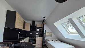 A compact kitchen with modern appliances, a dining area with a black table, and a bed with a white bedspread.