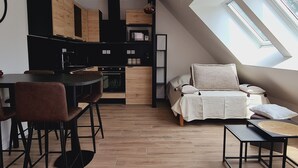 A compact kitchen with a dining area, a small sleeping area with a bed and pillows, and a skylight providing natural light.