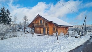 Een houten hutje met een sneeuwbedekte dak, omgeven door een besneeerd landschap en bomen.