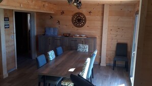 Een houten interieur met een eettafel, stoelen, een keukenhoek en een decoratieve wandklok.