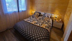 Een slaapkamer in een houten blokhut met een bed, twee bedlampen en een raam met gordijnen.