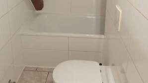Une petite salle de bain fermée, avec des toilettes blanches, une baignoire et des murs carrelés.