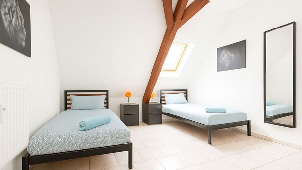 Une chambre avec deux lits, un grand miroir et une fenêtre de toit.