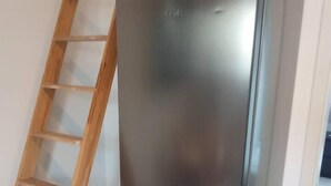 Un réfrigérateur en acier inoxydable dans une cuisine dont le sol est carrelé, avec une échelle en bois appuyée contre le mur.
