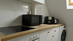 Une cuisine compacte équipée d’un four à micro-ondes, d’une machine à café et d’un lave-linge.