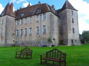 A large stone building with multiple windows and a central tower. There are two wooden benches in the foreground.