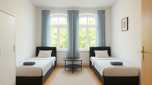 Ein Zimmer mit zwei Betten, einem kleinen Tisch und einem Fenster mit Vorhängen.