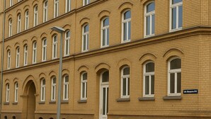 Ein mehrstöckiges Gebäude mit einer symmetrischen Fassade, das gleichmäßig verteilte Fenster und einen zentralen Eingang aufweist.