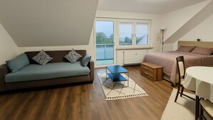En moderne stue med sofa, lille bord, seng og udsigt til det fri.